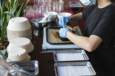 Kellnerin beim Einpacken von Essen auf einem Tablett im Restaurant während COVID-19 - PNAF01517