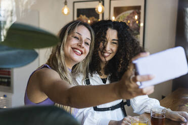 Cheerful young female friends taking selfie while sitting at restaurant - PNAF01521