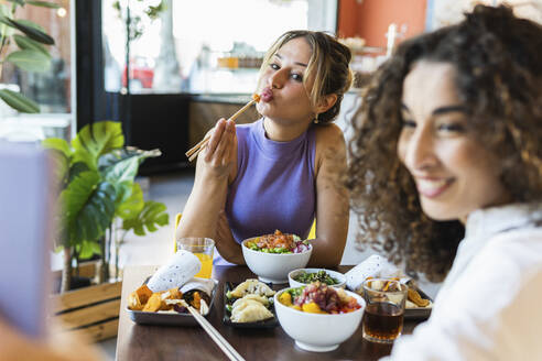 Junge Frau macht Selfie mit einer Freundin, die im Restaurant mit Stäbchen isst - PNAF01527