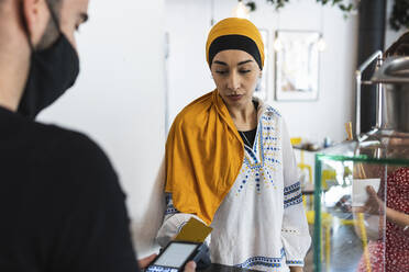 Junge Frau mit Kopftuch bezahlt mit Kreditkarte in einem Restaurant - PNAF01552