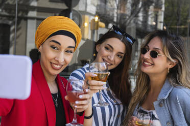 Junge Frau macht Selfie mit Freundinnen bei einem Drink - PNAF01555