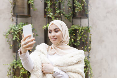 Junge Frau nimmt Selfie durch Handy vor der Wand - IFRF00516