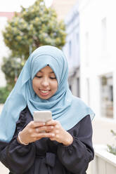 Junge Frau mit blauem Hidschab und Smartphone - IFRF00518