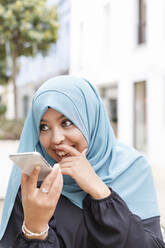 Glückliche junge Frau, die über einen Lautsprecher mit einem Mobiltelefon spricht - IFRF00519