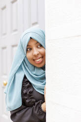 Lächelnde Frau mit Hidschab, die um die Wand lugt - IFRF00528