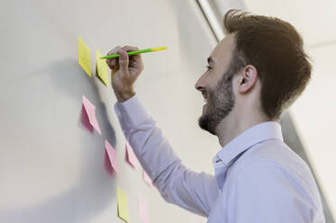 Happy businessman writing on adhesive notes at office - BMOF00560