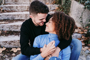 Young man holding hands while looking at smiling woman - EBBF03413