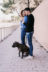 Young couple standing together with dog on footpath - EBBF03416