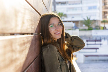 Smiling young woman leaning on wooded wall - DLTSF01840