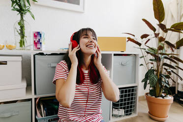 Lächelnde Frau hört Musik über Kopfhörer im Wohnzimmer - TCEF01809