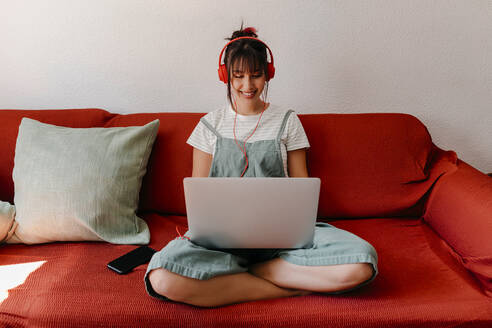 Woman with headphones working on laptop in living room - TCEF01825