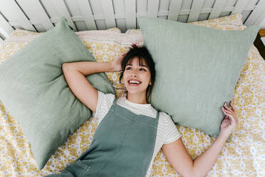 Nachdenkliche Frau lächelnd auf dem Bett liegend - TCEF01829