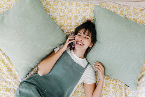 Beautiful woman talking on mobile phone while resting in bedroom - TCEF01830