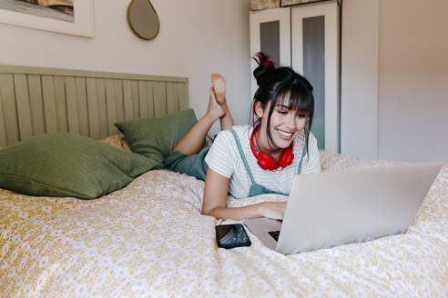 Frau lächelt, während sie einen Laptop auf dem Bett benutzt - TCEF01836
