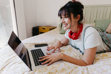 Lächelnde Frau arbeitet am Laptop im Schlafzimmer - TCEF01837
