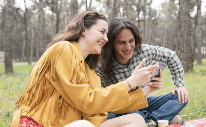 Cheerful man and woman looking at digital tablet during party in forest - JCCMF02120