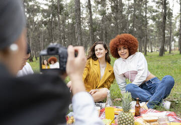 Male and female friends photographing while celebrating at forest - JCCMF02125