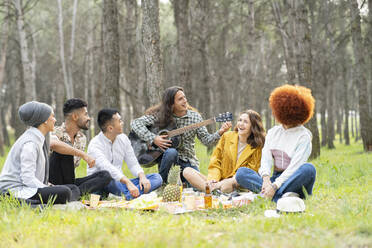 Junge männliche und weibliche Freunde spielen Gitarre beim Picknick im Wald - JCCMF02159