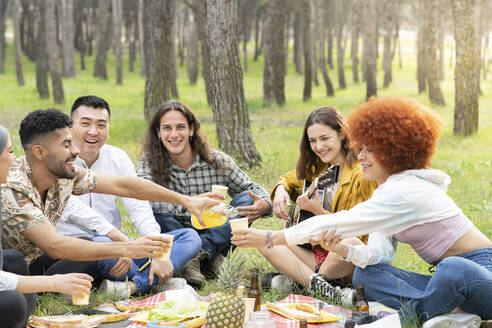 Cheerful male and female friends enjoying party in picnic at forest - JCCMF02166