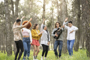 Multi-ethnic male and female friends enjoying while dancing in forest - JCCMF02180