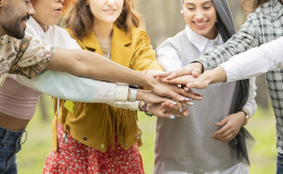 Multi-ethnic male and female friends stacking hands in forest during picnic - JCCMF02183