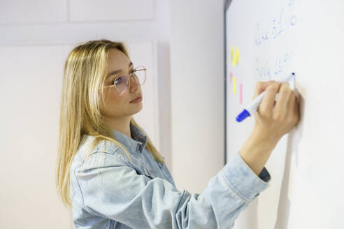 Blonde Geschäftsfrau, die in einer Besprechung im Büro auf ein Whiteboard schreibt - JSMF02132