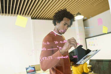 Afro hairstyle businessman writing on glass wall in office - JSMF02161