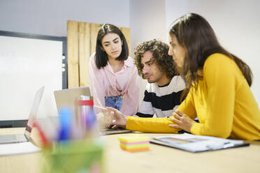 Multi-ethnic coworkers using laptop during meeting in office - JSMF02195