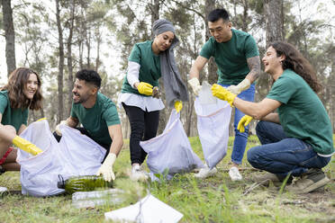 Lächelnde männliche und weibliche Freiwillige sammeln Plastik im Wald - JCCMF02192