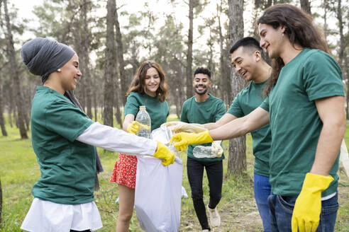 Multiethnische Freiwillige sammeln Müll in Plastiksäcken im Wald - JCCMF02195