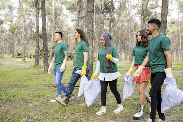 Male and female volunteers walking with garbage bag in forest - JCCMF02196