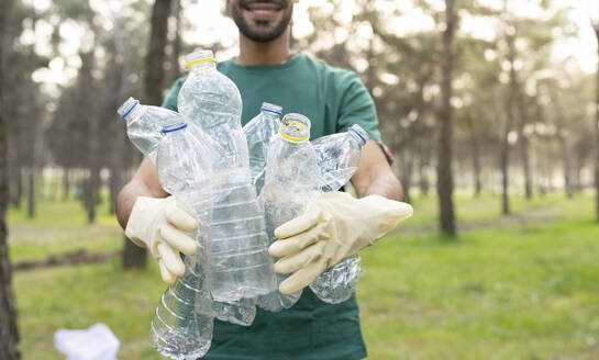 Männlicher Freiwilliger hält Plastikflaschen bei der Waldreinigung - JCCMF02201