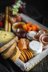 From above brunch box with assorted sliced meats various types of cheese and crispbreads arranged near ripe cup kiwi sweet strawberries and peeled mandarin near jam in glass jar on wooden table near napkin - ADSF23665