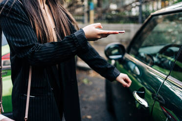 Unbekannte langhaarige Frau öffnet ein Auto mit Mobiltelefon - ADSF23696