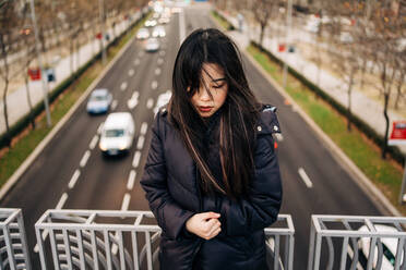 Long hair brunette asian woman standing on a bridge and looking down - ADSF23697