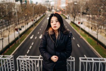 Langhaarige brünette asiatische Frau steht auf einer Brücke und schaut in die Kamera - ADSF23698