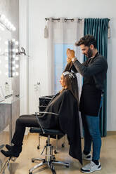 Side view of focused ethnic male master combing strands of female customer before dyeing in balayage technique - ADSF23754