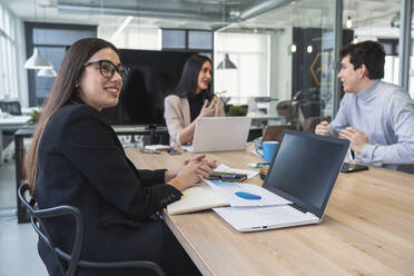 Businesswoman looking away while male and female colleague discussing at conference table in office - SNF01288