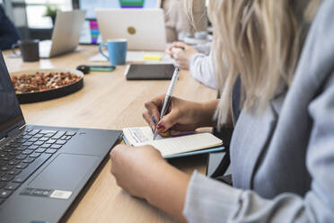 Geschäftsfrau schreibt während einer Besprechung vor einem Laptop im Büro Notizen in ihr Tagebuch - SNF01302