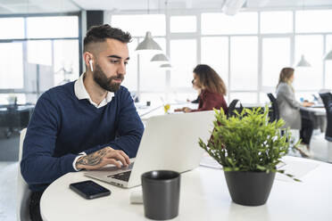 Male entrepreneur working on laptop with female colleagues in background at coworking office - SNF01306