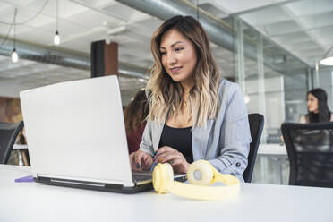 Lächelnde Unternehmerin mit Laptop am Schreibtisch in einem Coworking-Büro - SNF01320