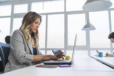 Geschäftsfrau arbeitet am Laptop am Schreibtisch im Coworking-Büro - SNF01323