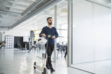 Geschäftsmann zu Fuß mit elektrischem Tretroller im Coworking-Büro - SNF01343