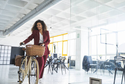 Junge Geschäftsfrau zu Fuß mit Fahrrad im Büro - SNF01346