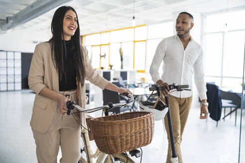 Lächelnde männliche und weibliche Unternehmer mit Fahrrädern in einem Coworking-Büro - SNF01356