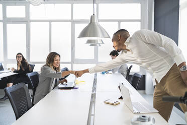 Lächelnde männliche und weibliche Unternehmer, die sich am Schreibtisch in einem Coworking-Büro die Fäuste stoßen - SNF01358