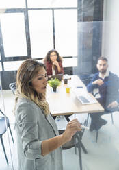 Businesswoman discussing business plan with male and female colleagues seen through glass at office - SNF01376