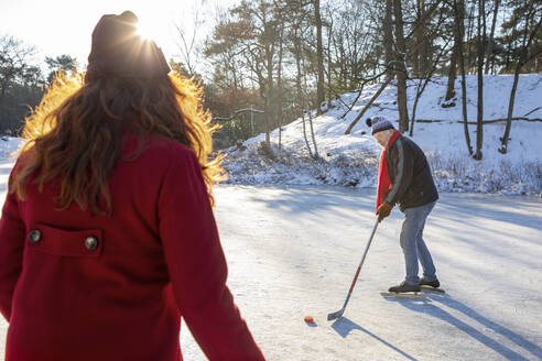 Älterer Mann spielt Eishockey mit Frau auf Schnee im Winter - FVDF00119