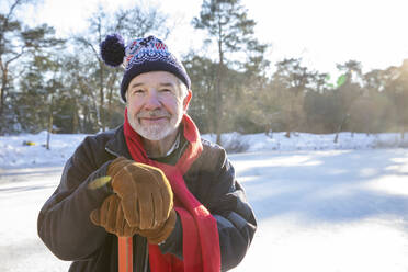 Senior man wearing gloves holding hockey stick outdoors - FVDF00125