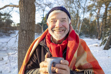 Lächelnder älterer Mann in Decke mit Kaffeetasse im Winter - FVDF00128